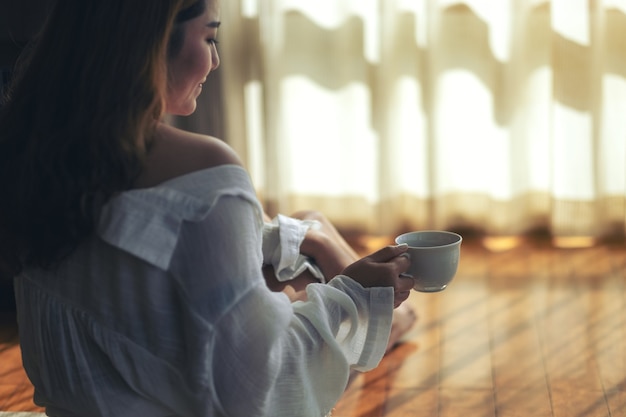 Uma mulher sentada no chão segurando uma xícara de café quente para beber pela manhã