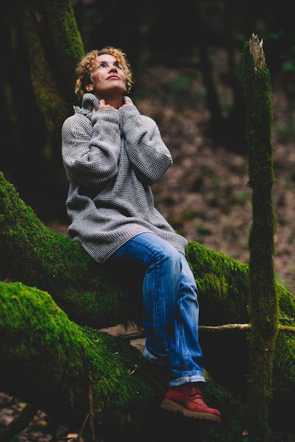 Uma mulher serena e feliz sentada em um tronco de árvore selvagem verde olhando para cima e desfrutando da sensação de conexão com a natureza meio ambiente e floresta florestal destino de viagem pessoas feliz senhora turista ao ar livre