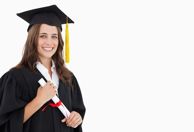 Uma mulher sorridente com um diploma na mão enquanto olha para a câmera