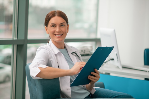 Uma mulher sorridente com uma túnica branca segurando uma lista de receitas e parecendo satisfeita