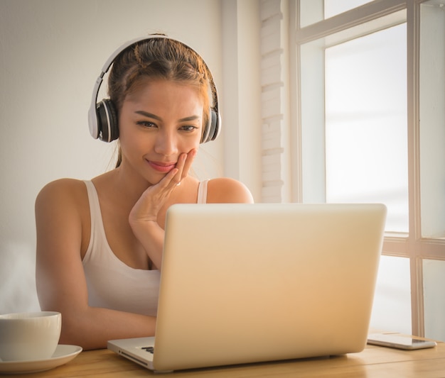 Foto uma mulher tailandesa de blusa sem mangas está trabalhando com um notebook on-line em sua sala.