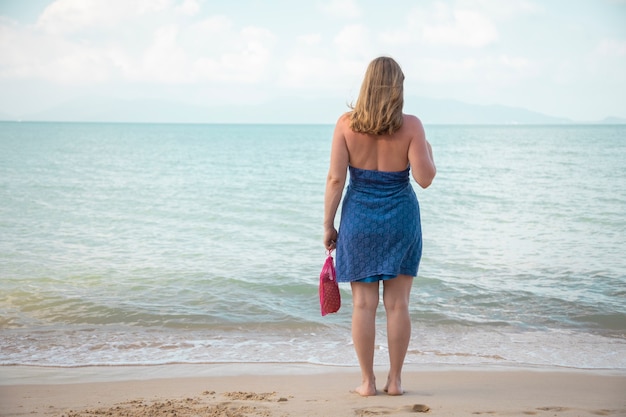 uma mulher tem na mão uma sacola de compras de malha e fica à beira-mar em uma praia arenosa. conceito de ecologia. consumo consciente