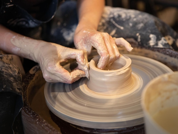 Uma mulher trabalha na roda de oleiro As mãos formam uma xícara de barro molhado na roda de oleiro Conceito artístico