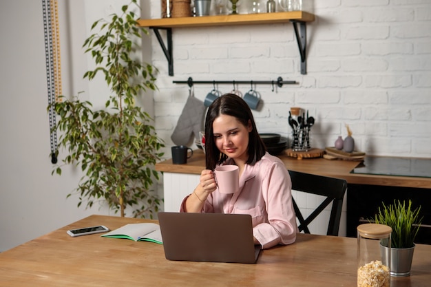 Uma mulher trabalha no escritório, remotamente de casa, na cozinha, sentada diante do computador. Ensino à distância, educação online e trabalho. Aluna se prepara para os exames.