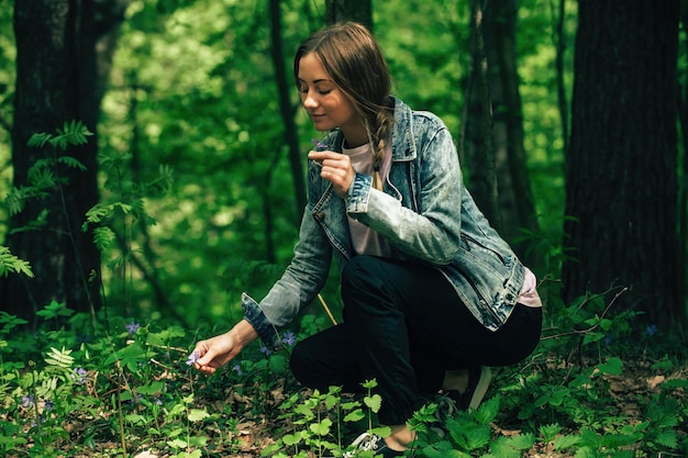 uma mulher turista caminha pela floresta verde na estação quente e admira as flores da floresta