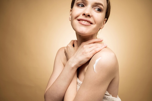 Uma mulher usa um creme e um esfoliante para hidratar a pele do corpo