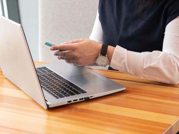 Uma mulher usa um smartphone enquanto está sentada na frente de um laptop em roupas de escritório Trabalho on-line remoto
