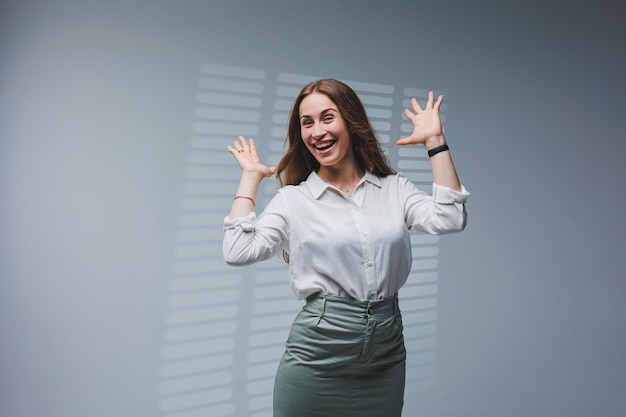 Uma mulher usa uma blusa branca e saia em um fundo cinza emoções no rosto de uma mulher elegante olhar positivo mulher modelo em roupas casuais primavera verão ou outono look de rua