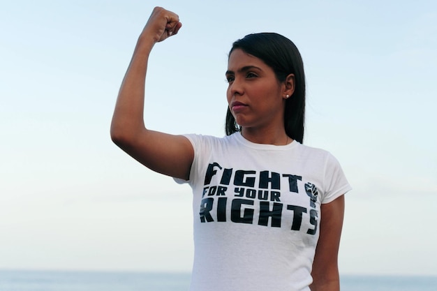 Uma mulher usa uma camiseta com um slogan feminista e levanta o punho no ar.