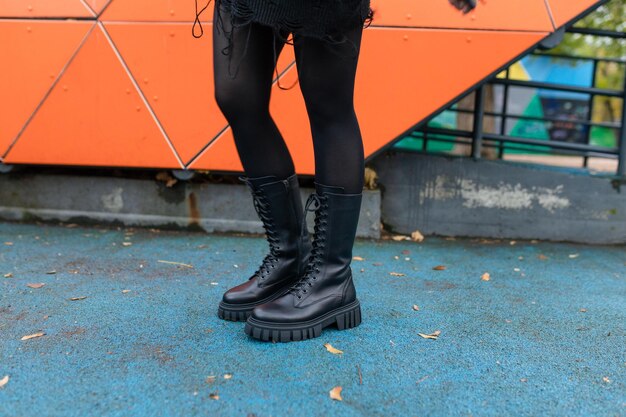 Foto uma mulher usando botas de combate pretas está em frente a uma parede laranja.