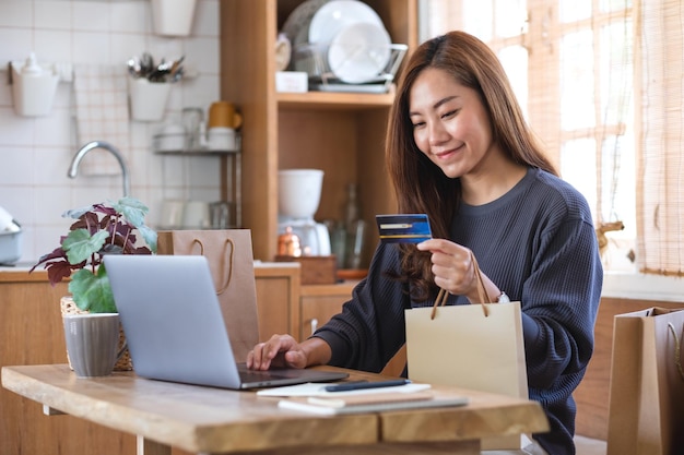 Uma mulher usando computador portátil e cartão de crédito para compras online em casa