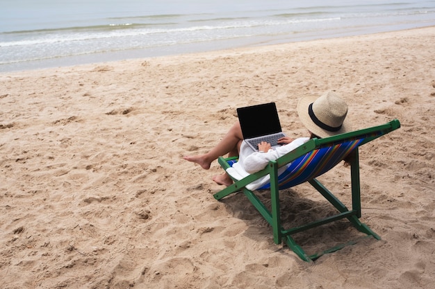 Uma mulher usando e digitando em um laptop enquanto está deitada em uma cadeira de praia