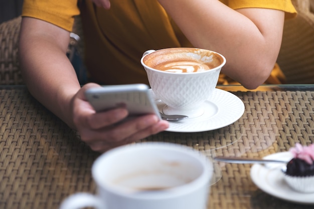 uma mulher usando e olhando para o telefone inteligente com xícaras de café no café