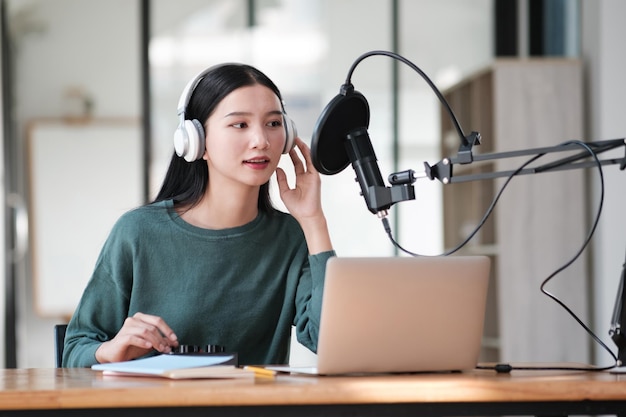 Uma mulher usando fones de ouvido está sentada em uma mesa com um laptop e um microfone