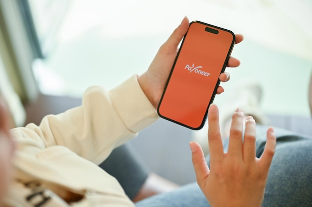 Uma mulher usando o aplicativo Payoneer em seu smartphone iPhone com o logotipo do aplicativo Payoneer na tela