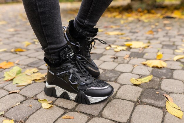 Uma mulher usando sapatos pretos com cadarços pretos fica em um caminho de pedra nas folhas de outono.