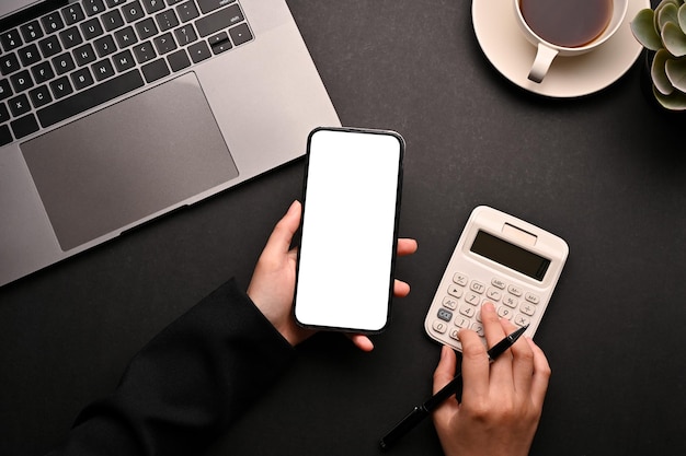 Uma mulher usando smartphone e calculadora em sua visão superior da mesa de escritório preto moderno