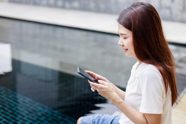 Uma mulher usando um smartphone durante as férias perto da piscina em um hotel resort