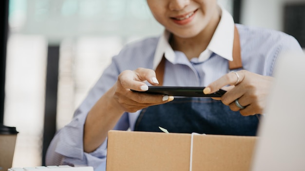 Uma mulher usando um smartphone para tirar fotos na frente de caixas de encomendas caixas de encomendas para embalar mercadorias entregando mercadorias por meio de empresas de correio privado Venda online e conceitos de compras online