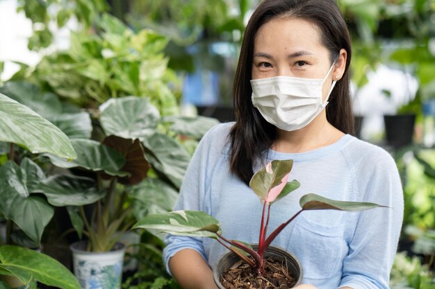 Uma mulher usando uma máscara facial segura um vaso de plantas em uma estufa.