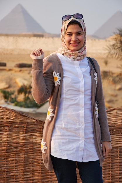 Uma mulher vestindo um cardigã marrom com margaridas está em frente a um cenário de deserto.