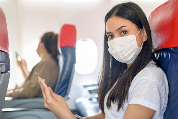 Uma mulher viajando usando máscara protetora a bordo do livro de leitura da aeronave, viagens sob pandemia covid-19, viagens de segurança, protocolo de distanciamento social, novo conceito de viagem normal