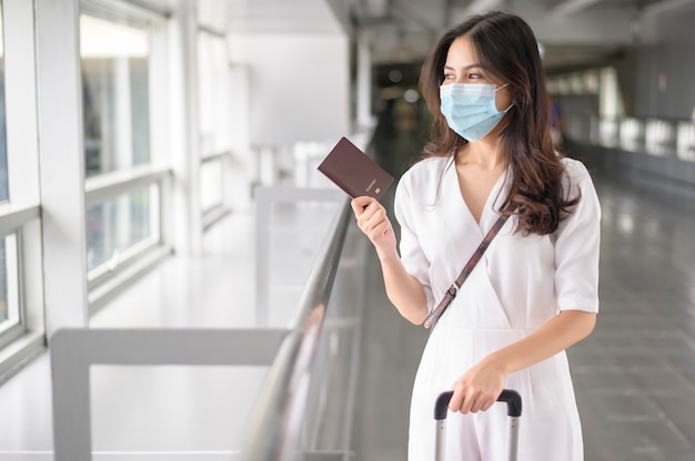 Uma mulher viajante está usando máscara protetora no aeroporto internacional, viagem sob a pandemia de Covid-19, viagens de segurança, protocolo de distanciamento social, novo conceito de viagem normal.