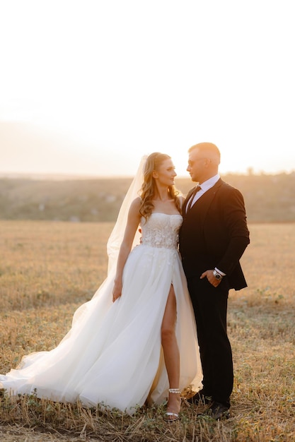 uma noiva e um noivo posam em um campo ao pôr do sol