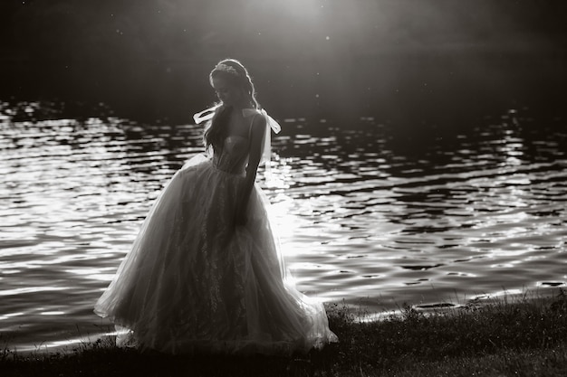 Uma noiva elegante em um vestido branco aprecia a natureza ao pôr do sol. Modelo em um vestido de noiva na natureza no Parque. foto preto e branco
