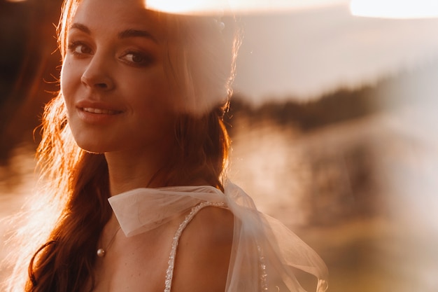 Uma noiva elegante em um vestido branco aprecia a natureza ao pôr do sol. Modelo em um vestido de noiva na natureza no parque.