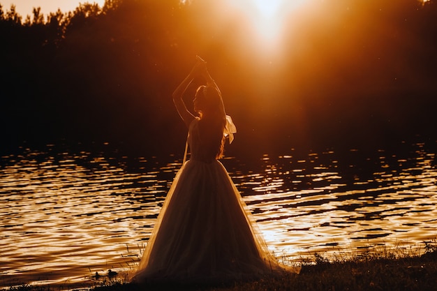 Uma noiva elegante em um vestido branco aprecia a natureza ao pôr do sol. Modelo em um vestido de noiva na natureza no parque.