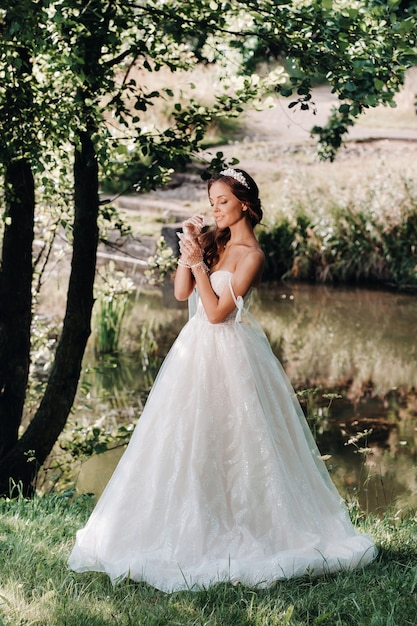 Uma noiva elegante em um vestido branco, luvas com um buquê em uma cachoeira no parque