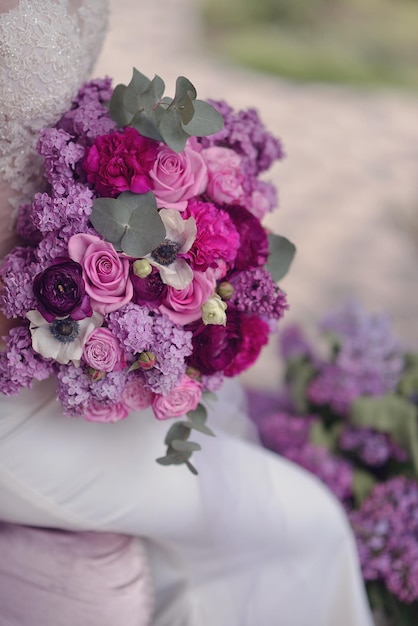 Uma noiva em um vestido branco segura um buquê de flores roxas.