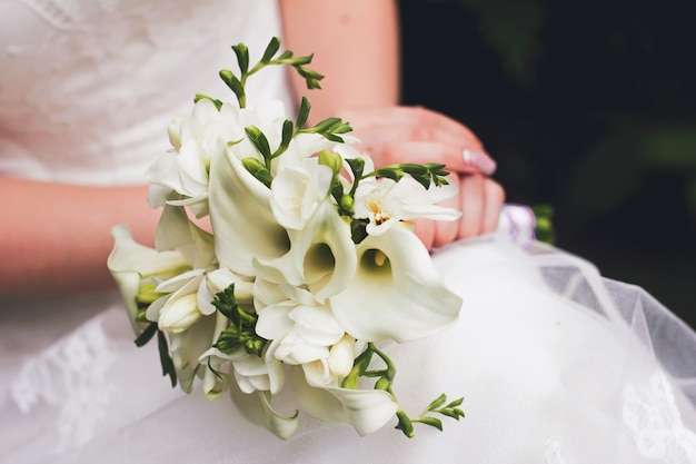 Uma noiva em um vestido de noiva branco segura um buquê de lírios brancos