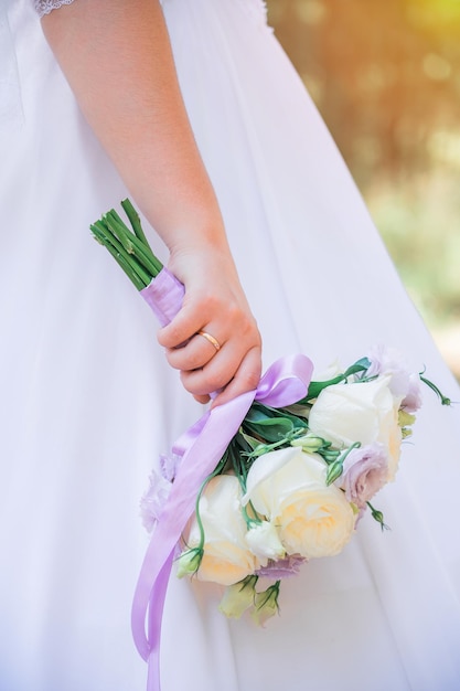 Uma noiva em um vestido de noiva segura um buquê de rosas brancas e cravos lilás