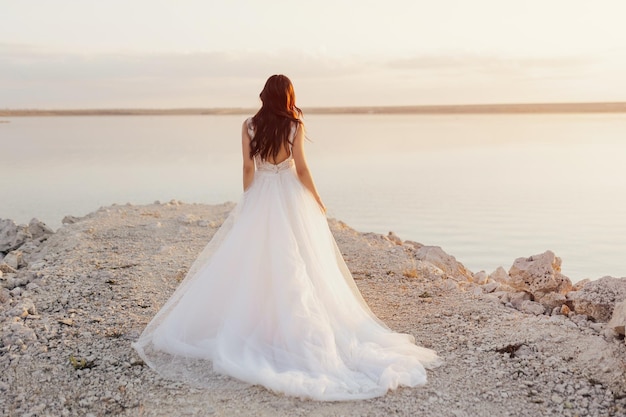 Uma noiva está em uma praia olhando para o mar.