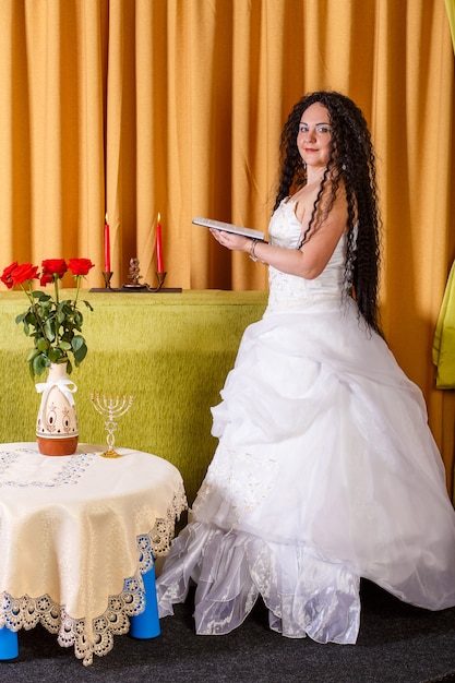 Uma noiva judia em um vestido de noiva branco sem véu lê as orações Tegilim na sala antes da cerimônia chupá. Foto vertical