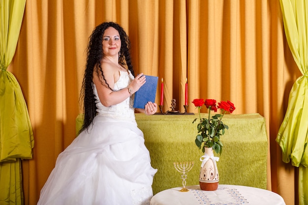 Uma noiva judia em um vestido de noiva branco sem véu segura um livro fechado de tegilim em suas mãos antes da cerimônia chupa. foto horizontal