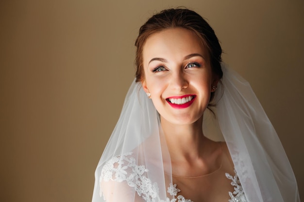 Uma noiva linda com um sorriso sincero em um vestido de véu branco posa e se prepara para a cerimônia de casamento