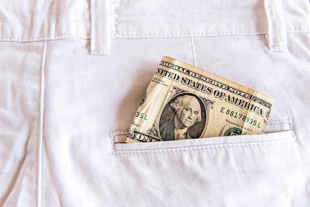 Uma nota de dólar dobrada no bolso da calça jeans branca