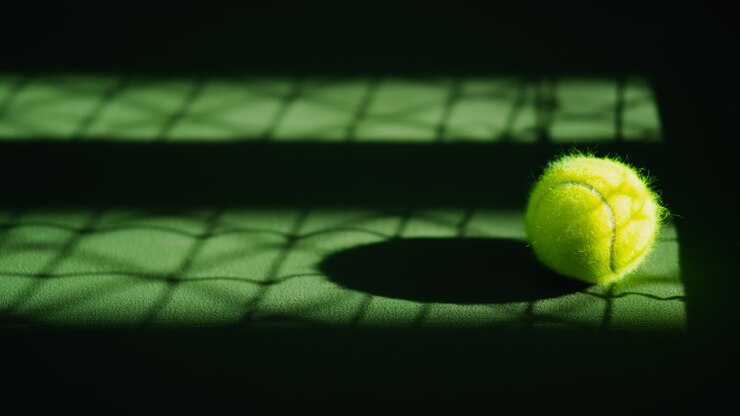 Uma nova bola de tênis e sombra líquida na quadra dura verde com luz da direita