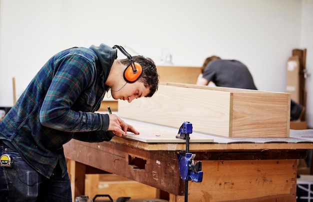 Uma oficina de móveis fazendo peças de móveis contemporâneos sob medida usando habilidades tradicionais em design moderno Um homem marcando um pedaço de madeira com um lápis