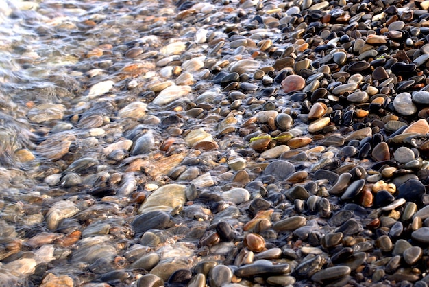 Uma onda do mar transparente pura rola sobre a costa de seixos rochosos o conceito de descanso e viagem tranquilidade relaxamento e reflexão em um dia quente de verão closeup