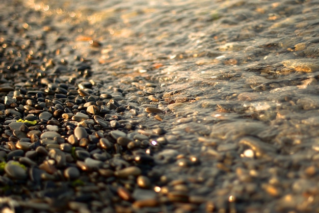 Uma onda do mar transparente rola sobre uma praia de seixos, recreação e viagens, desfocagem, bokeh.