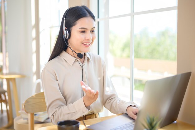 Uma operadora de atendimento ao cliente usando um fone de ouvido usando o computador, atendendo chamadas de clientes no escritório