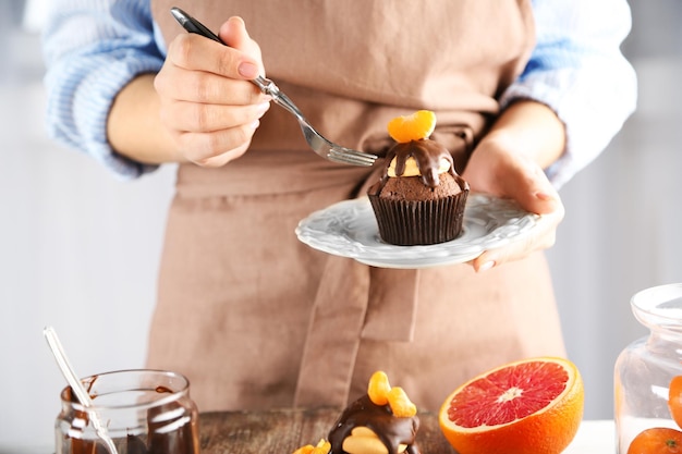 Uma padeira decora um delicioso cupcake com uma fatia de mandarina e chocolate na mesa