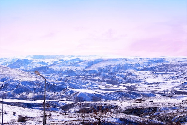 Uma paisagem de neve com um céu rosa e uma cordilheira nevada ao fundo.