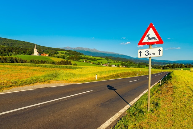 Uma paisagem rural austríaca com uma estrada vazia entre campos agrícolas que levam aos Alpes