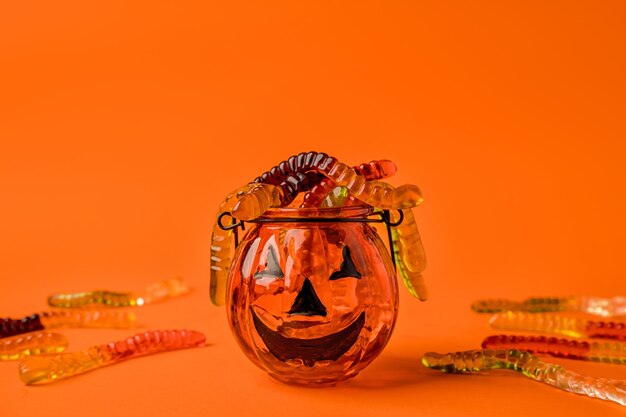 Uma panela em forma de abóbora está cheia de minhocas de geléia em um conceito de fundo laranja de Hallowee