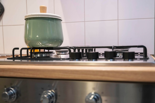 Uma panela verde clara com tampa fica em um fogão a gás doméstico cozinhando em casa